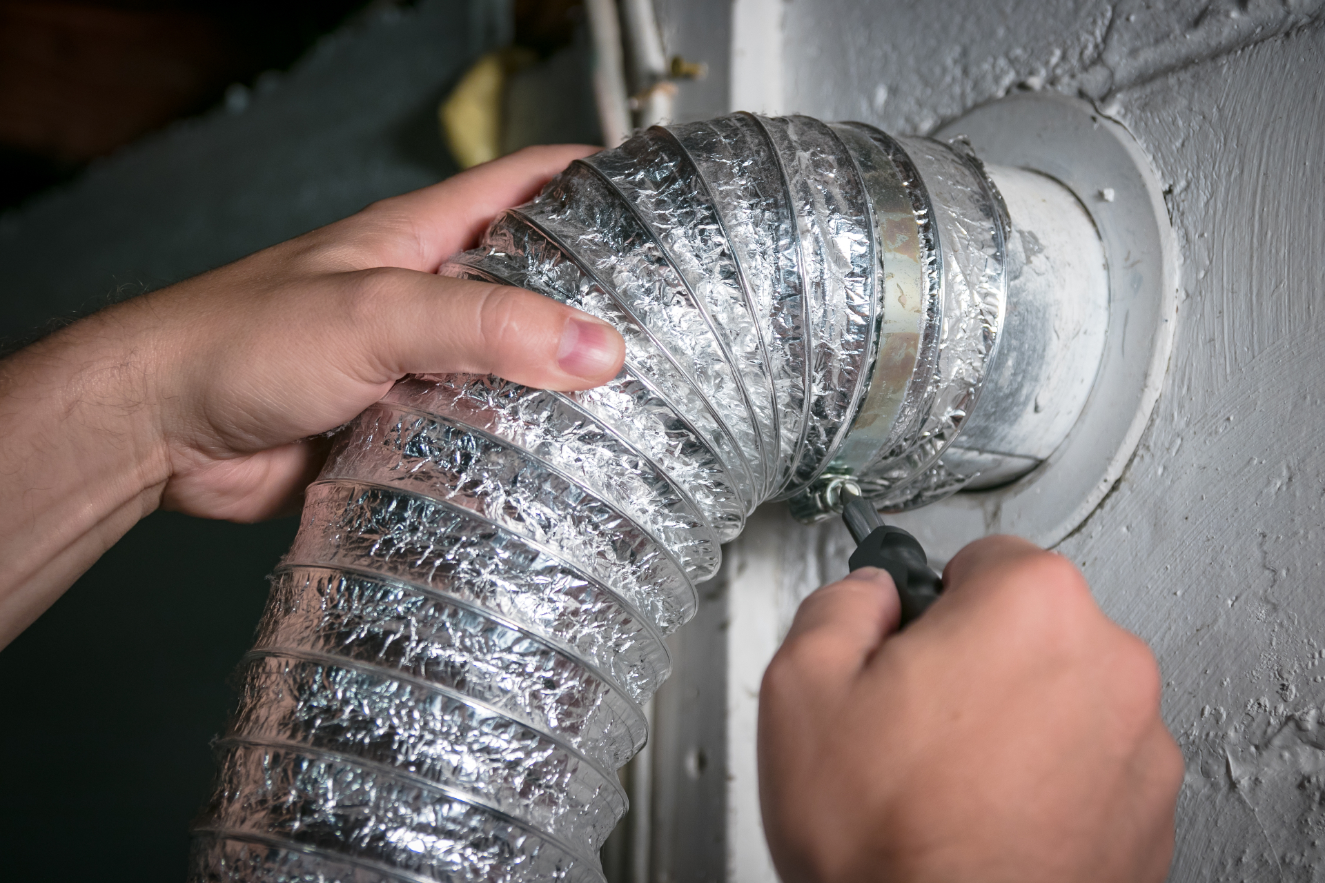 Dryer Vent Squad technician rerouting a flexible dryer vent line at the wall connection